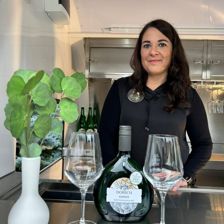 Frau mit Flasche Alkohol und Gläsern auf einer Bartheke, dekoriert mit einer Pflanze.